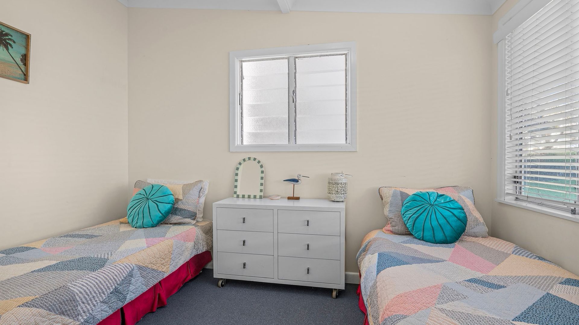 Une chambre avec deux lits, une commode, une fenêtre et un tableau accroché au mur.