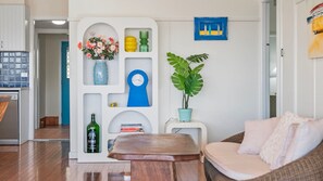 Ein modernes Wohnzimmer mit weißer Wand, einer blauen Uhr, einer Topfpflanze und einem Couchtisch aus Holz.