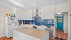 A kitchen with white cabinets, a blue-tiled backsplash, a stainless steel range hood, and a built-in dishwasher. - Fairview – A Classic Crescent Head Escape (Crescent Head)
