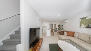 A modern apartment with a staircase, a flat-screen TV, a sofa, a dining area, and a kitchen. - Breakwall Retreat - Harrington (Harrington)