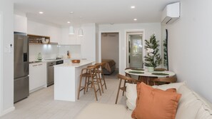 A modern kitchen with white cabinets, a stainless steel refrigerator, and a dining area with a round table and wooden chairs. - Breakwall Retreat - Harrington (Harrington)