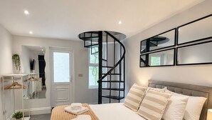 A modern bedroom with a curved staircase, a bed with a beige blanket, and a bedside table with a lamp. - Hyde Park Premium Duplex Apartment (London)