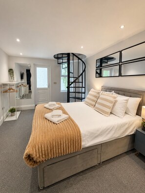 A modern bedroom with a curved staircase, a bed with a beige blanket, and a bedside table with a lamp. - Hyde Park Premium Duplex Apartment (London)