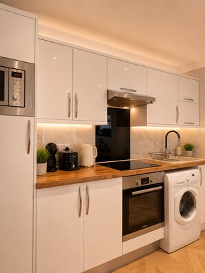 A modern kitchen with white cabinetry, stainless steel appliances, and a wooden countertop. - Hyde Park Premium Duplex Apartment (London)