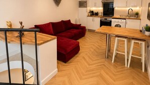 A modern kitchen with white cabinets, a red sofa, and a wooden dining table. - Hyde Park Premium Duplex Apartment (London)