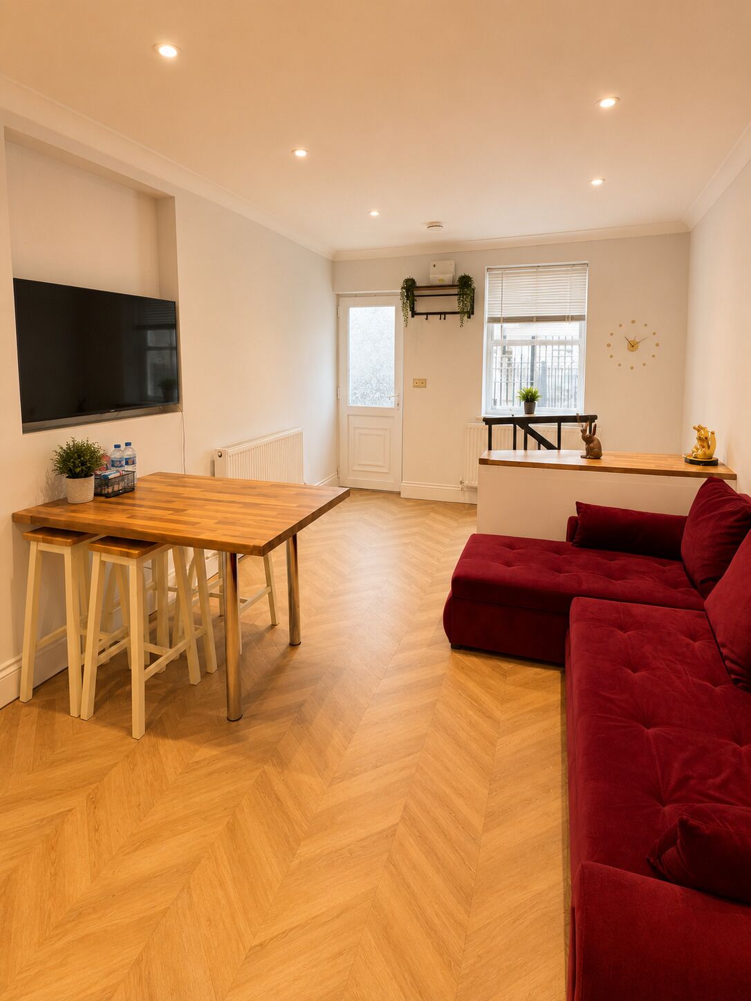 A modern living space with a wooden dining table, red sofa, and a TV mounted on the wall.
