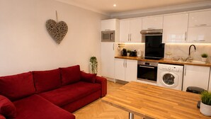 A modern kitchen with white cabinets, a red sofa, and a wooden dining table. - Hyde Park Premium Duplex Apartment (London)