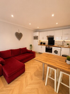 A modern kitchen with white cabinets, a red sofa, and a wooden dining table. - Hyde Park Premium Duplex Apartment (London)