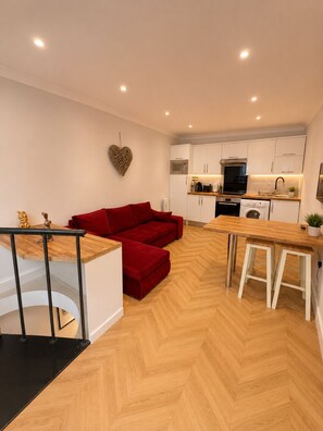 Eine moderne Küche mit weißen Schränken, einem roten Sofa und einem Holzes Esstisch.