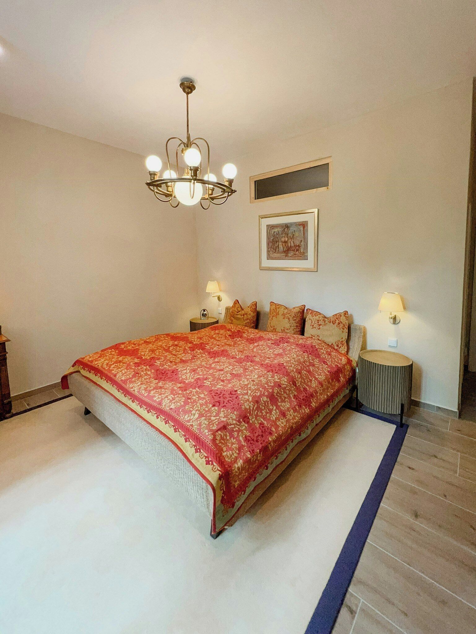 Ein Schlafzimmer mit einem großen Bett, einer Chandelier, zwei Nachttischen mit Lampen und einem gerahmten Bild an der Wand.