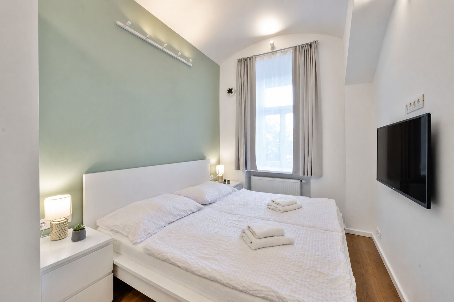 Una habitación de hotel con cama, mesitas de noche, televisor y ventana con cortinas.