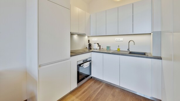 Una cocina moderna con armarios blancos, horno empotrado, pileta y una encimera con diversos electrodomésticos.