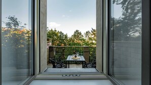 Un balcón con mesa y sillas, vistas a árboles y edificios, y cielo despejado.