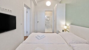 Una habitación de hotel con cama, televisor montado en la pared, lámpara de noche y puerta que da a un baño.