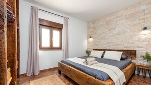 Ein Schlafzimmer mit einem hölzernen Bett, einer Steinwand, einem Fenster mit Vorhängen und einem Nachttisch mit Lampe.