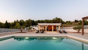 Ein moderner Poolbereich mit klarem Pool, Liegestühlen und einem Gebäude mit offener Terrasse.