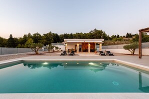 Ein moderner Poolbereich mit klarem Pool, Liegestühlen und einem Gebäude mit offener Terrasse.