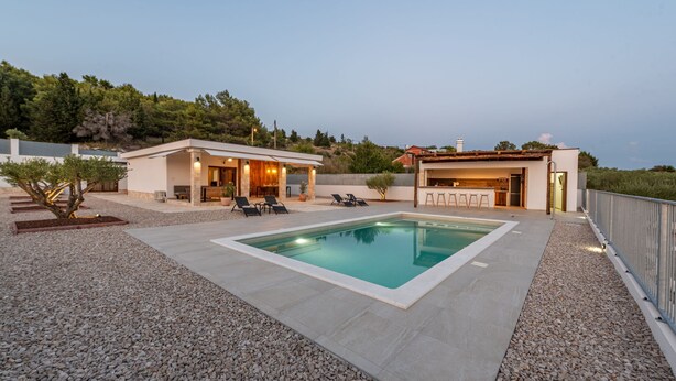 Ein moderner Außenpoolbereich mit einem rechteckigen Pool, Liegestühlen und einer Bar.