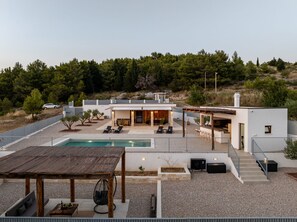 Ein modernes Haus mit Swimmingpool, Sitzgelegenheiten im Freien und Blick auf einen bewaldeten Hang.