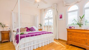 Un dormitorio con cama con dosel, cómoda de madera y un ventanal con vistas.