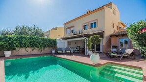 Una casa de dos pisos con piscina, mobiliario exterior y un porche cubierto.