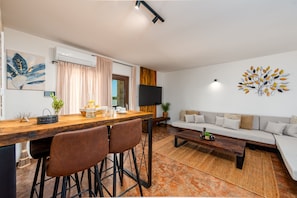 Un espacio habitable moderno con comedor, un conjunto de sofás y un televisor montado en la pared.
