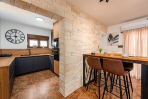 Eine moderne Küche mit einer Wand aus Stein, einer Holz Arbeitsplatte und einer Bar mit Hockern.