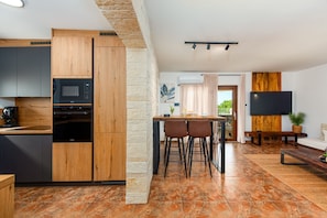 A modern kitchen with built-in appliances, a dining area with a table and chairs, a flat-screen TV, and a living area with a sofa and a coffee table. - Villa Casa Olea ZadarVillas (Perušic Benkovacki)