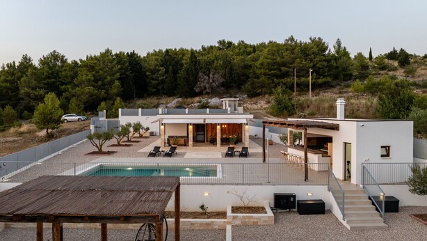 Una casa moderna con piscina, mobiliario de exterior y vistas a una ladera boscosa.
