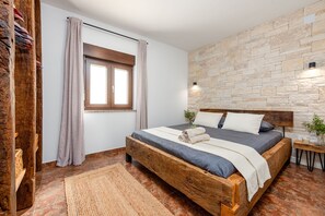 Ein Schlafzimmer mit einem hölzernen Bett, einer Steinwand, einem Fenster mit Vorhängen und einem Nachttisch mit Lampe.