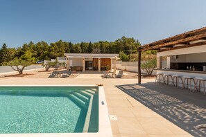 Ein Poolbereich mit klarem Pool, Liegestühlen und einer Bar.