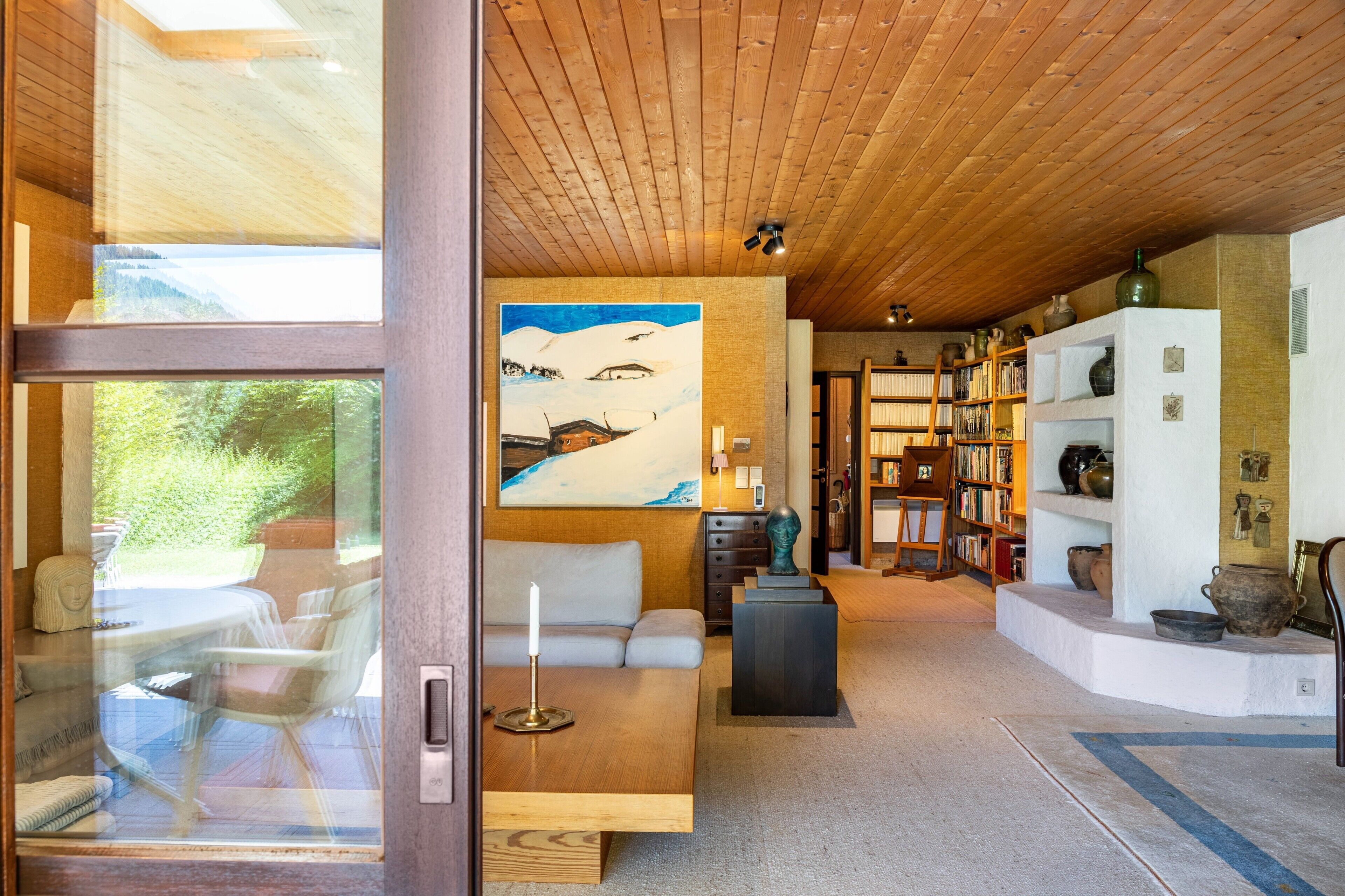 Un intérieur moderne avec un plafond en bois, un tableau, un canapé, une table et une bibliothèque.