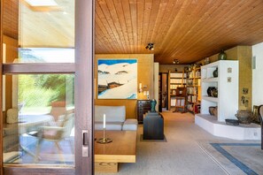 Un interno moderno con soffitto in legno, un quadro, un divano, un tavolo e una libreria.