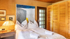 A bedroom with a bed, pillows, a nightstand with a lamp, a door with frosted glass panels, and a wooden wardrobe. - Villa “Mona Lisa” with Mountain Views, Private Terrace, and Wi-Fi (Seefeld)