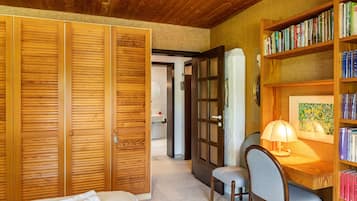 Una stanza con pannelli di legno, una libreria, una scrivania con una lampada, una sedia e un letto con un asciugamano arrotolato.