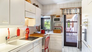 A compact kitchen with white cabinets, a microwave, a stove, and a red chair. - Villa “Mona Lisa” with Mountain Views, Private Terrace, and Wi-Fi (Seefeld)