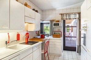 Een kleine keuken met witte kastjes, een magnetron, een fornuis en een rode stoel.