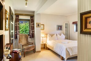 Une chambre d’hôtel avec un lit, une chaise, une table de chevet, une lampe et une fenêtre avec des rideaux.