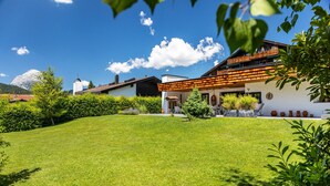 A modern house with a well-maintained lawn, a wooden deck, and a mountain backdrop. - Villa “Mona Lisa” with Mountain Views, Private Terrace, and Wi-Fi (Seefeld)