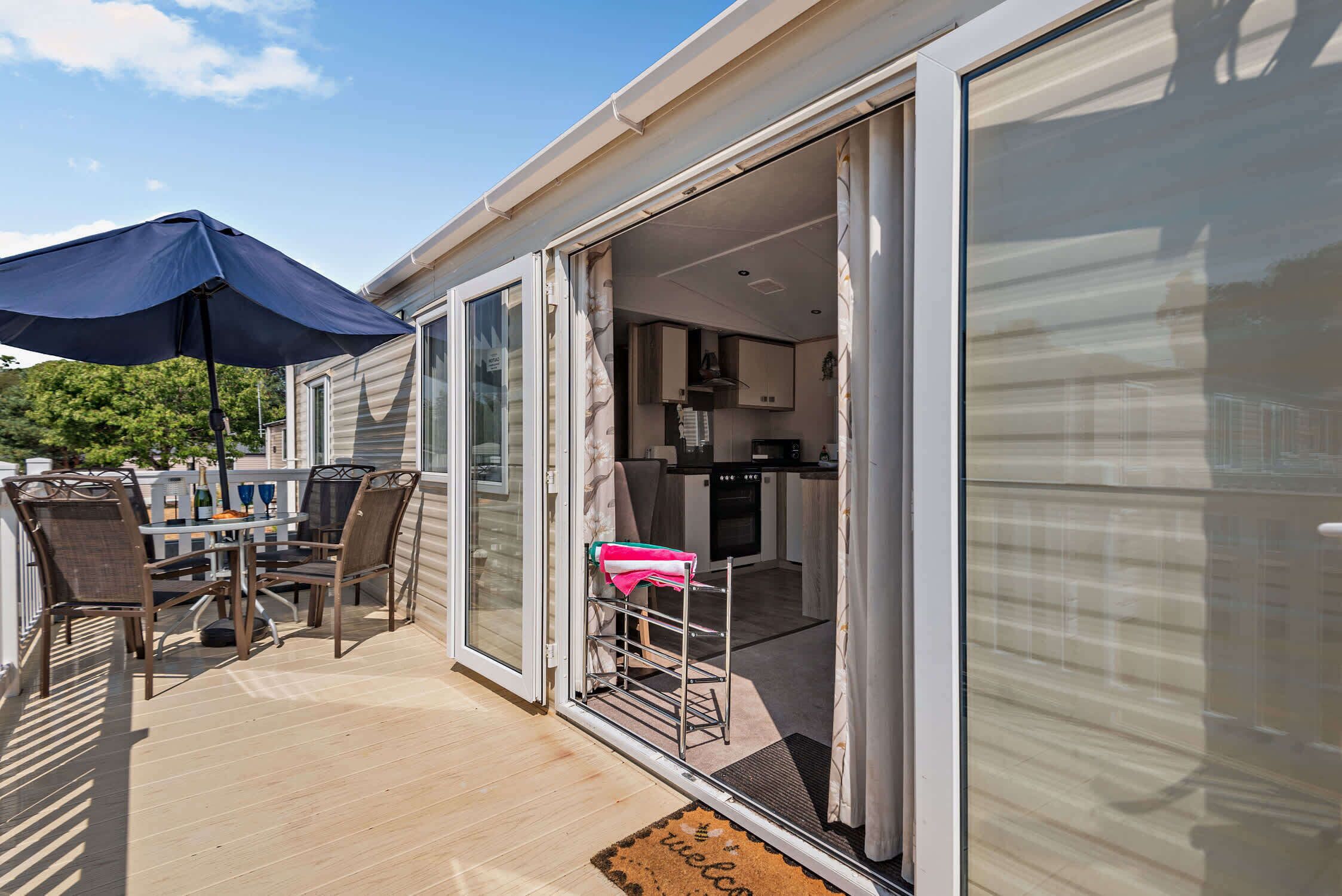 A covered patio with a table and chairs, a sliding glass door leading to a kitchen, and a doormat with a welcome message.