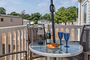 Ein Glastisch mit einer Champagnerflasche, zwei blauen Gläsern und einem Croissant auf einem Balkon mit Geländer.