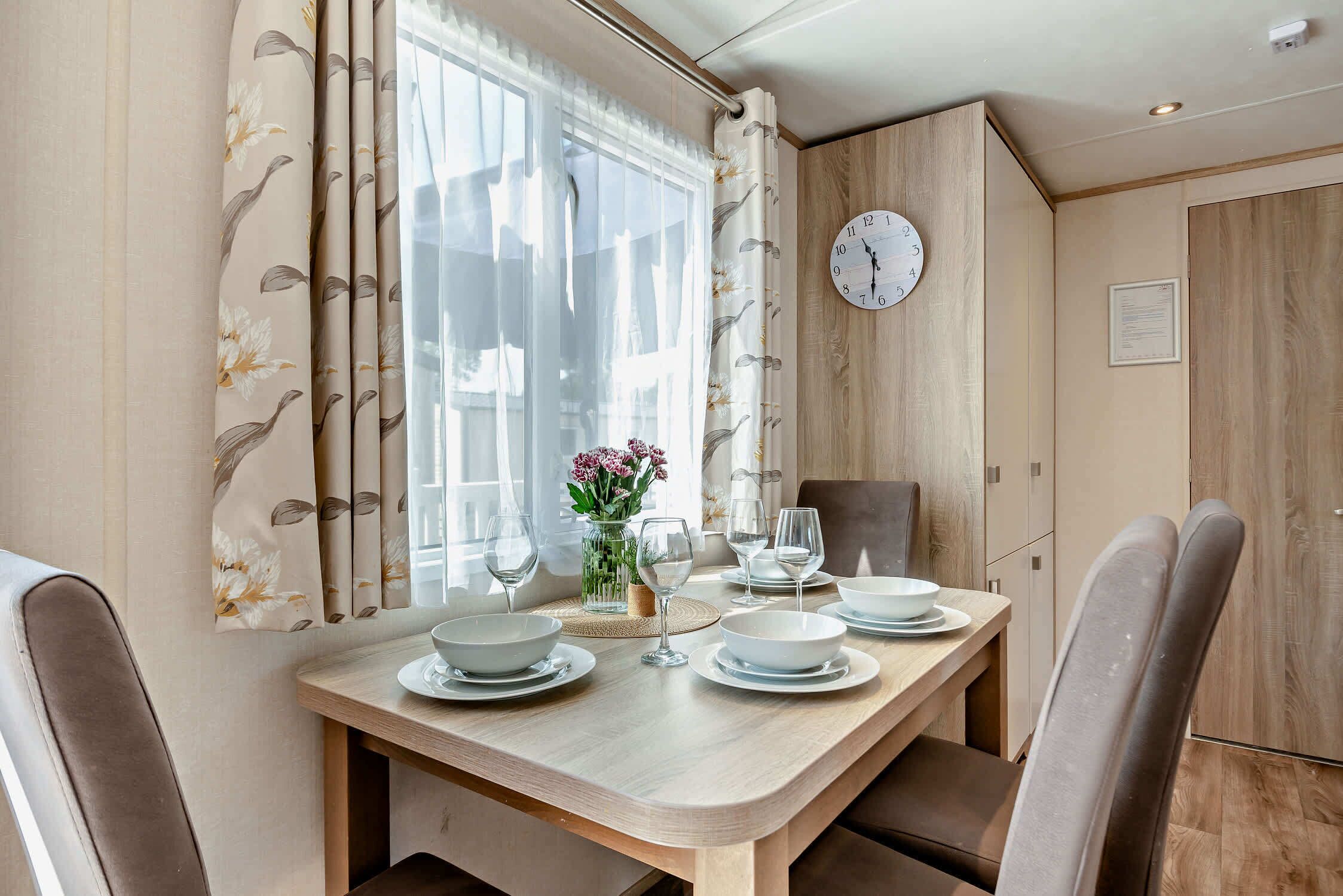 Un comedor con una mesa de madera, sillas, un reloj y un jarrón con flores.