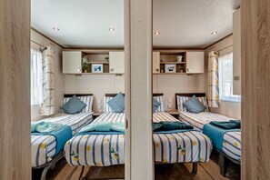 Ein Zimmer mit Spiegel, ausgestattet mit vier Betten, jeweils mit gestreifter Bettwäsche und Kissen, sowie einer zentralen Regaleinheit mit verschiedenen Gegenständen.