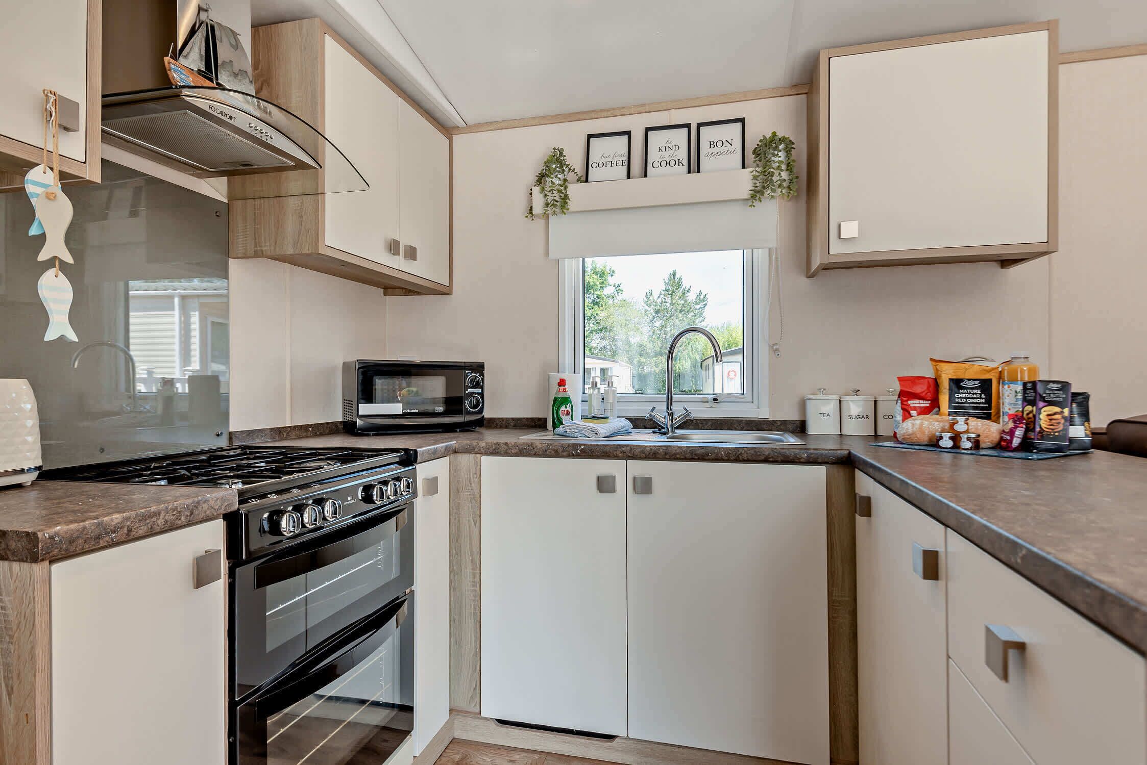 A modern kitchen with a stove, oven, microwave, and a sink. There are cabinets, a window with a view, and kitchen decor.