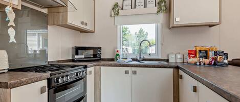 A modern kitchen with a stove, oven, microwave, and a sink. There are cabinets, a window with a view, and kitchen decor.