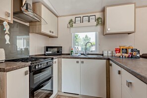 Une cuisine moderne équipée d’une cuisinière, d’un four, d’un four à micro-ondes et d’un évier. On y trouve également des placards, une fenêtre avec vue et des éléments de décoration.