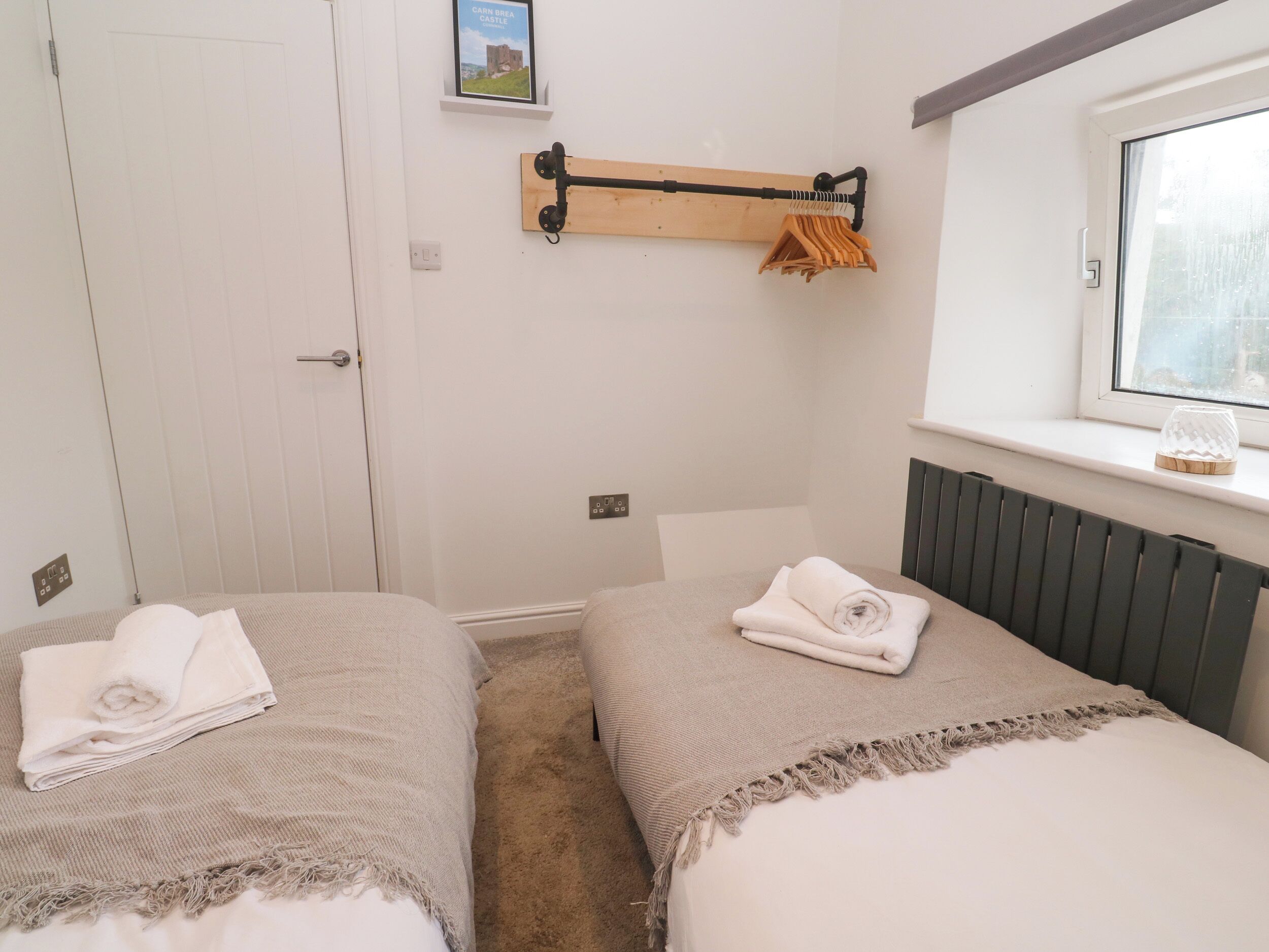 A bedroom with two beds, a window, a radiator, and a towel rack.