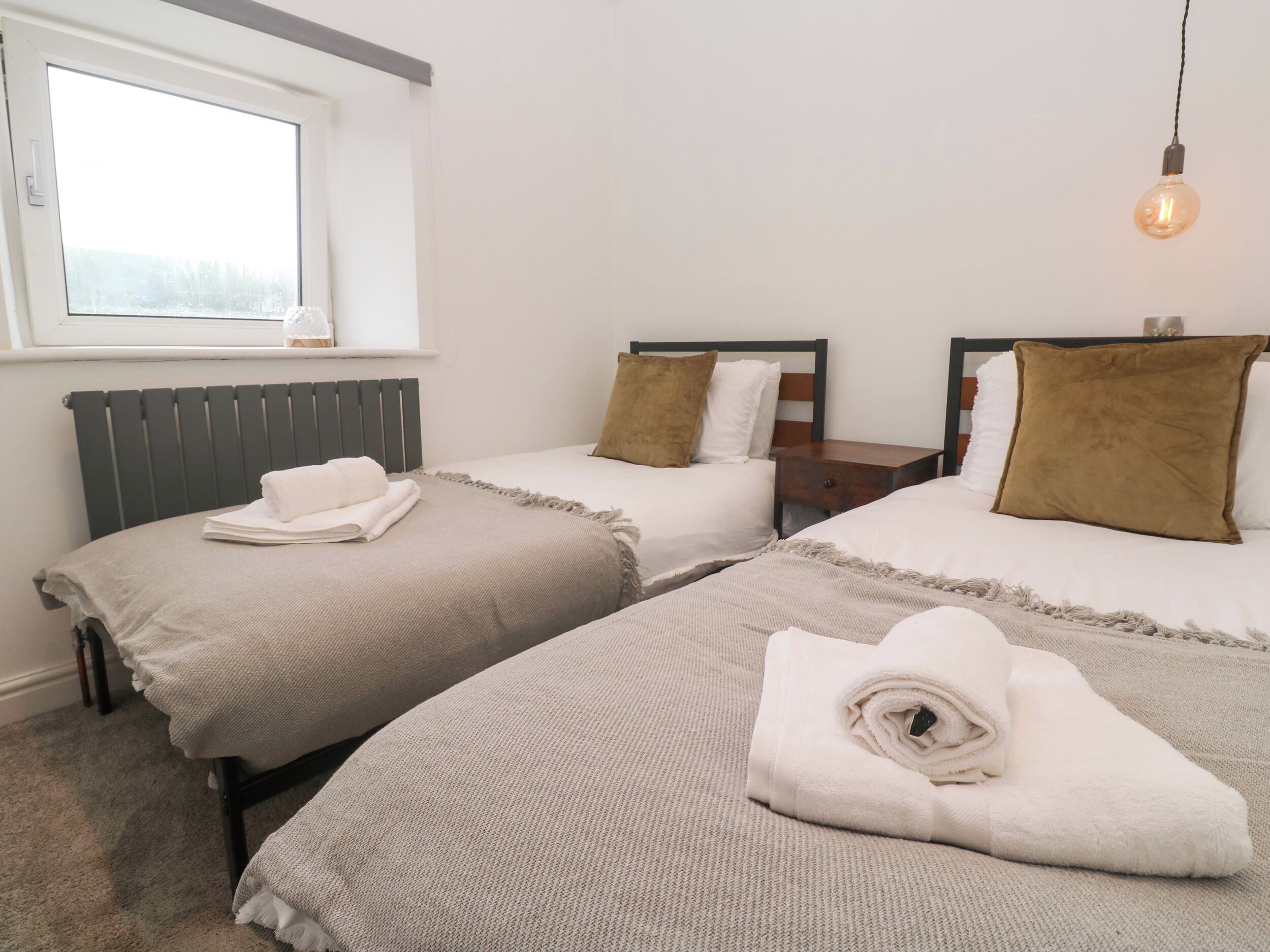Habitación de hotel con dos camas, una ventana, un radiador y una bombilla colgante.