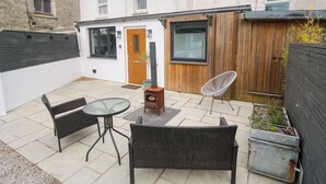Un patio con mobiliario de mimbre, un estufa de leña y una puerta de madera.