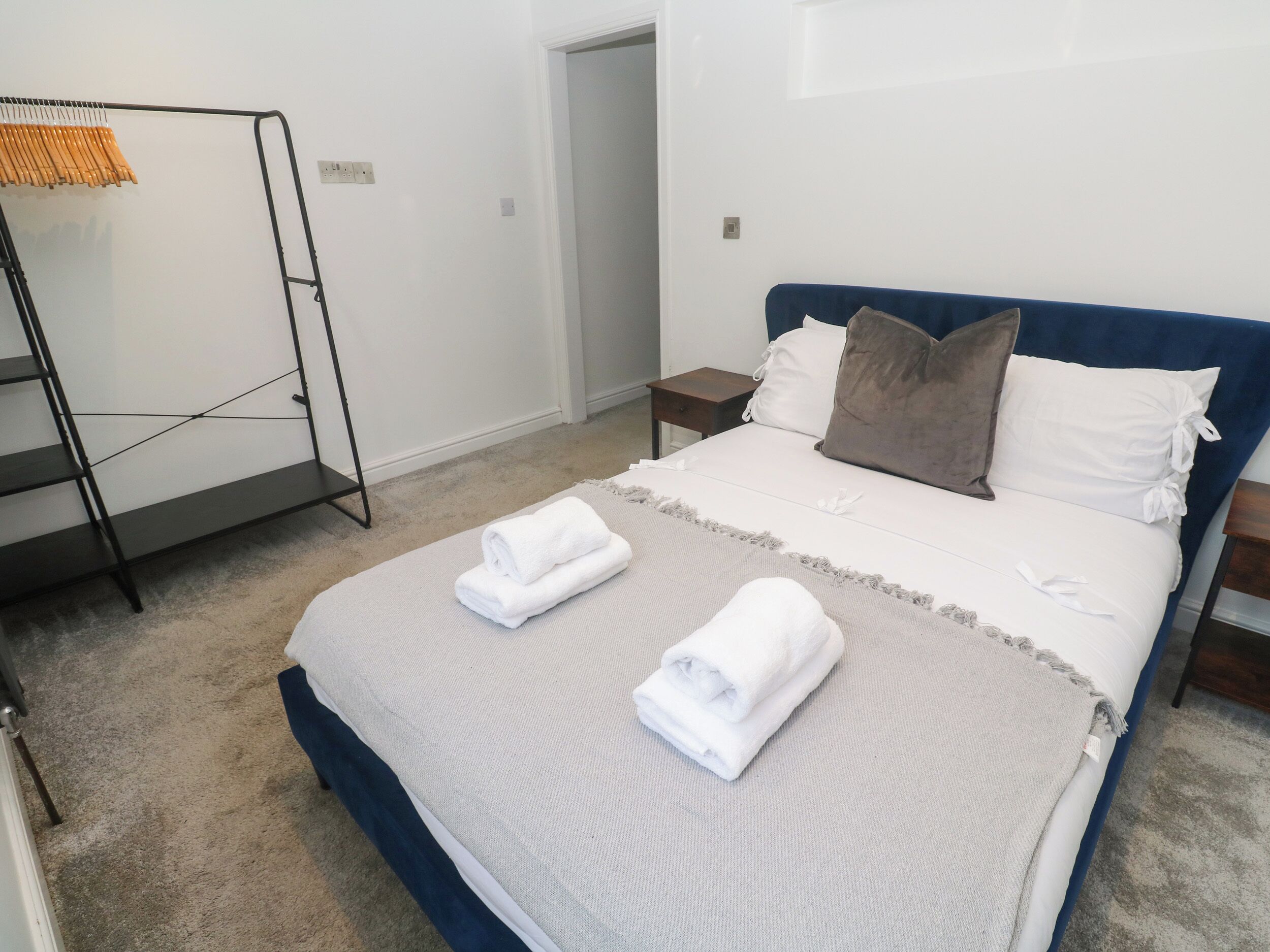 A neatly made bed with a blue headboard, white pillows, and a folded white towel on the bed.
